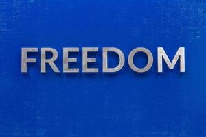 the word freedom laid with silver metal characters on blue painted wooden board in central flat lay composition