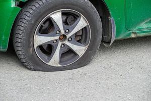 old green civil car flat tire close-up at dry sunny day on gray asphalt surface photo