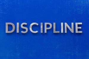 la palabra disciplina colocada con caracteres de metal plateado en una tabla de madera pintada de azul en una composición plana central foto