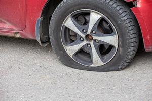 old red civil car flat tire close-up at dry sunny day on gray asphalt surface photo