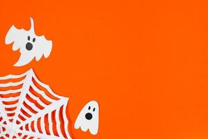 Halloween concept. Festive decorations - paper ghosts and spider web on orange background. photo