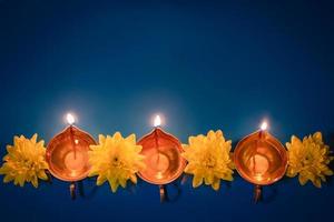Happy Diwali. Diya oil lamps and yellow flowers on blue background. Celebrating the traditional Indian holiday of light. photo