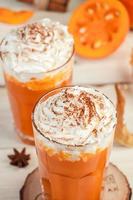 Pumpkin latte with whipped cream on light wooden background. Hot spicy smoothie. Vegetable vegan drink. photo