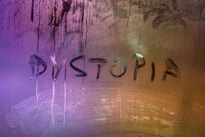 the word dystopia handwritten on wet window glass surface photo