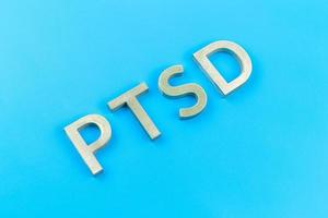 abreviatura ptsd - trastorno de estrés postraumático - colocado con letras de metal plateado sobre una superficie plana azul foto