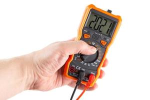 digit 2021 on lcd screen of digital electrical multimeter in left hand, isolated on white background photo