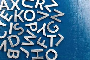 maqueta plana de caracteres alfabéticos de metal plateado sobre fondo de tablero pintado de azul con espacio de copia.