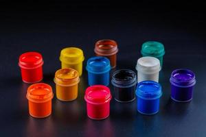 close-up background of opened small gouache paint jars on black surface photo