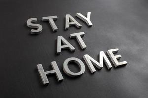 the words stay at home laid with brushed aluminium letters on matte black background in diagonal perspective photo