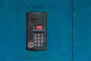 An intercom on old painted blue steel surface with a keypad, digital display and rfid sensor for calling close-up photo