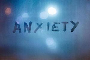 the word anxiety written by finger on night wet glass with blurred classic blue lights in background photo