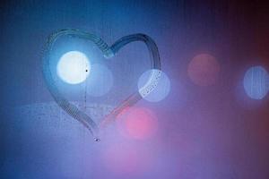 símbolo del corazón dibujado a mano en el cristal de la ventana de la noche húmeda en colores azules foto