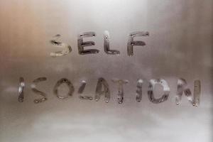 the words self isolation handwritten on wet window glass at daytime - close-up full frame picture with selective focus photo