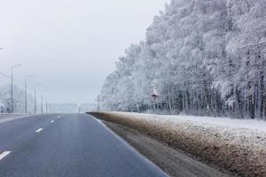 winter road among frosted forest at daylight with no cars on it photo