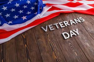 the words veterans day laid with silver metal letters on wooden board surface with crumpled usa flag photo