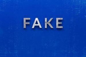 the word fake laid with silver metal characters on blue painted wooden board in central flat lay composition photo
