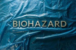 la palabra riesgo biológico colocada con letras plateadas sobre fondo azul de película plástica arrugada en composición plana en el centro foto