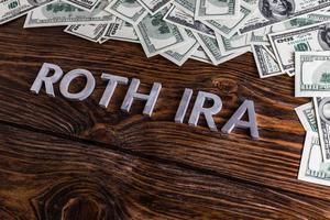 words ROTH IRA laid on wooden surface with metal letters and us dollar banknotes photo