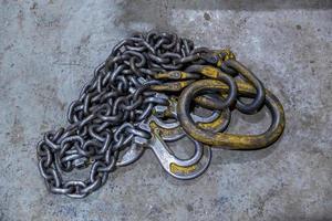 old industrial crane chain lays on concrete floor with rings and hooks photo