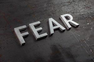 the word fear laid with silver letters on raw rusted steel sheet surface in diagonal slanted perspective photo