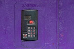 An intercom on purple painted red steel surface with a keypad, digital display and rfid sensor for calling close-up photo