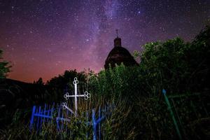 Abandoned christian grave under ruins of church at starry night with visible milky way galaxy. photo