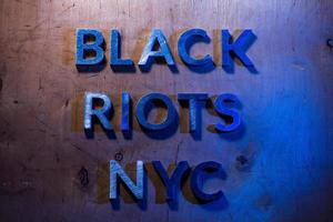 The words black riots NYC laid with metal letters on flat plywood surface under white and blue police lights. Concept. photo