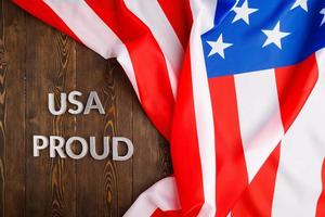 words USA proud laid with silver letters on brown wooden surface with US flag photo