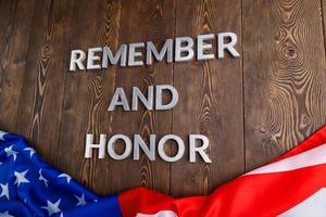 las palabras recuerdan y honran colocadas con letras de metal plateado sobre fondo de madera con la bandera de EE.UU. debajo foto