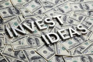 The words INVEST IDEAS with thick metal letters on the US dollar bills background - with selective focus photo