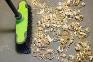 a small pile of wood shavings on a gray linoleum floor with a broom brush photo