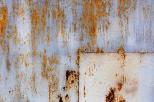 rusted flat solid sheet metal surface with leftovers of white and light blue paint, with rectangular patch in the corner photo