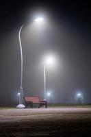 bench in night misty park with tall lights and selective focus photo