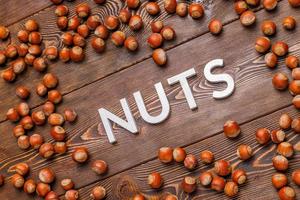 the word nuts laid with silver letters on wooden board background surrounded with scattered hazelnuts photo