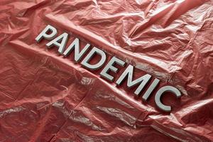 la palabra pandemia se colocó con letras plateadas en una película plástica roja arrugada - composición de perspectiva diagonal con enfoque selectivo foto