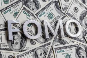 The word FOMO laid with aluminium letters on the US dollar banknotes background - with selective focus photo