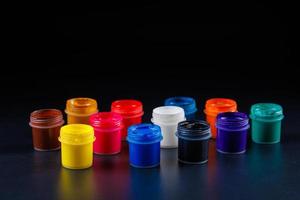 close-up background of opened small gouache paint jars on black surface photo