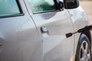 hand with high pressure washer washing white car at public self service car washing station photo