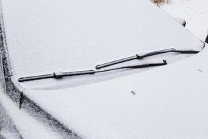 parabrisas de coche y limpiaparabrisas congelados y cubiertos de nieve a la luz del día nublado de invierno foto