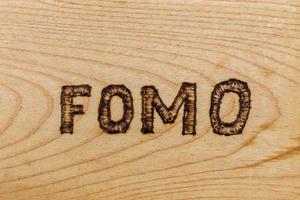 abbreviation FOMO - fear of missing out - burnt by hand on flat wooden surface photo