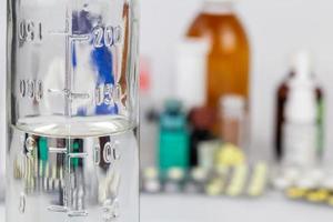 measuring bottle glass bottle with colorless liquid on blurred meds background with selective focus photo