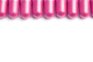 row of plastic pink color organic capsules isolated on white background closeup with selective focus photo