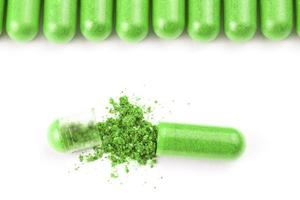 row of ufo green color organic capsules isolated on white background closeup with one opened photo