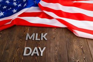 la palabra mlk day colocada con letras de metal plateado sobre una superficie de madera con una bandera de estados unidos arrugada en la parte superior foto