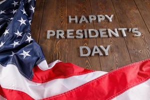 palabras feliz día de los presidentes colocadas con letras reales en una tabla de madera cerca de la bandera estadounidense foto