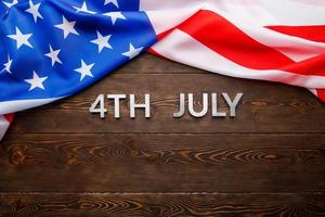 the words 4th july and crumpled usa flag on flat textured wooden surface background photo