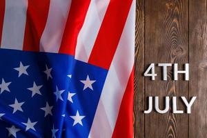 las palabras 4 de julio y la bandera de estados unidos arrugada sobre fondo de superficie de madera con textura plana foto