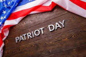 the words patriot day laid with silver metal letters on wooden board surface with crumpled usa flag photo