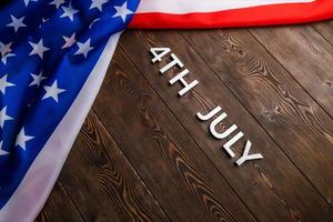 the words 4th july and crumpled usa flag on flat textured wooden surface background photo