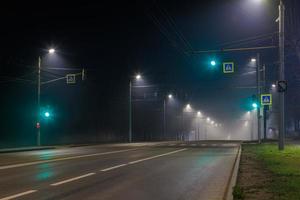 empty foggy night road with rows of lamp posts, green traffic light and pedestrian crossing photo